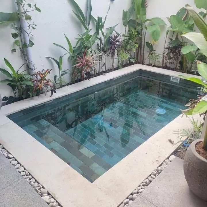 Finished plunge pool with green stone tiles, a pebble border and potted plants