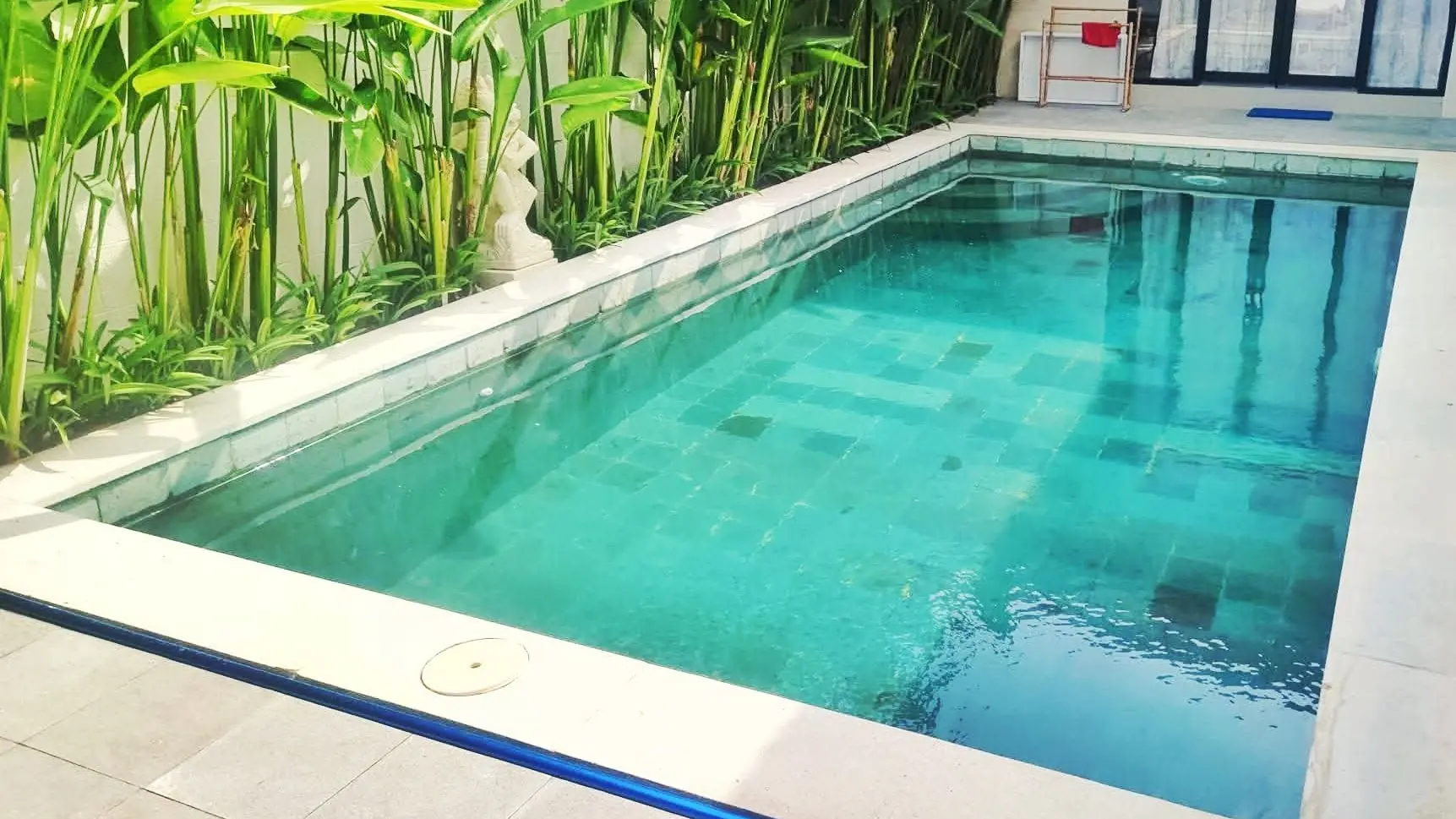Completed long swimming pool with green stone tiles and tropical plants in Sanur, Bali