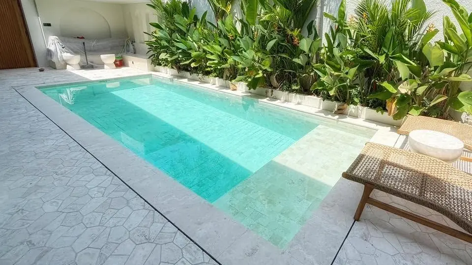 Pool with a shallow ledge, light stone paving and tropical planting